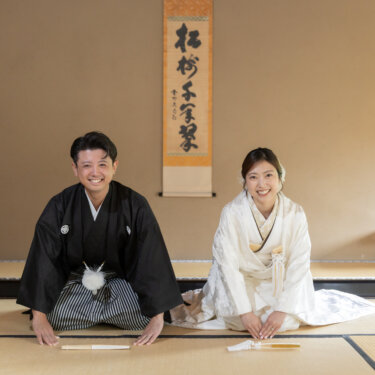 Couple in shiromuku and black montsuki seated formally on tatami with folded fans placed before them, a classic portrait for kimono wedding photos in Japan
