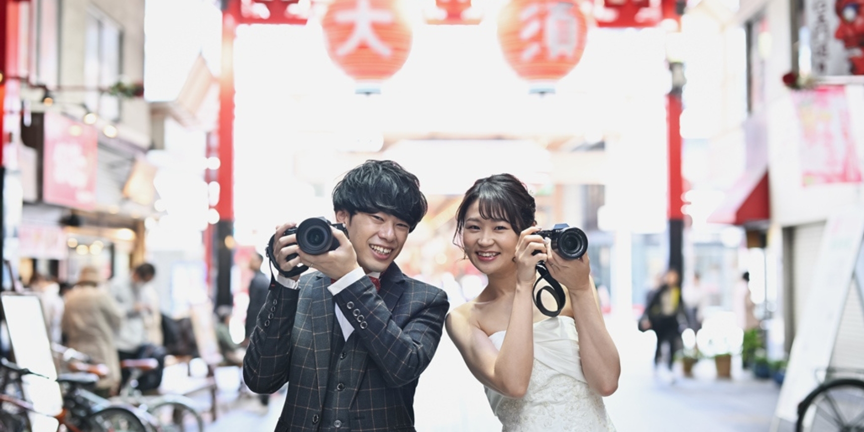 Couple laughing while holding cameras beneath a red lantern gate in the lively Osu shopping arcade.