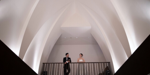 Bathed in soft ambient lighting beneath a vaulted white ceiling, the couple stands together in one of six available chapel venues.