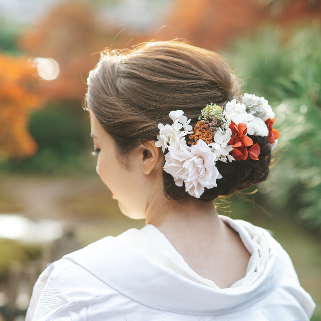 A bridal updo adorned with soft white, red, and orange dried flowers, paired with a white kimono shawl.