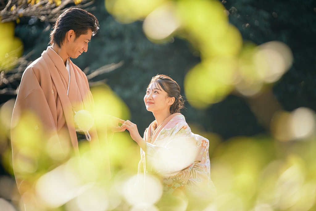 The couple shares a tender moment through a veil of golden green leaves in dappled sunlight.