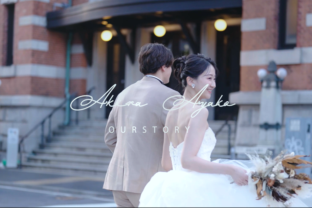 Video still reading 'Akira Ayako Our Story', couple walking together in front of a grand brick building at dusk.