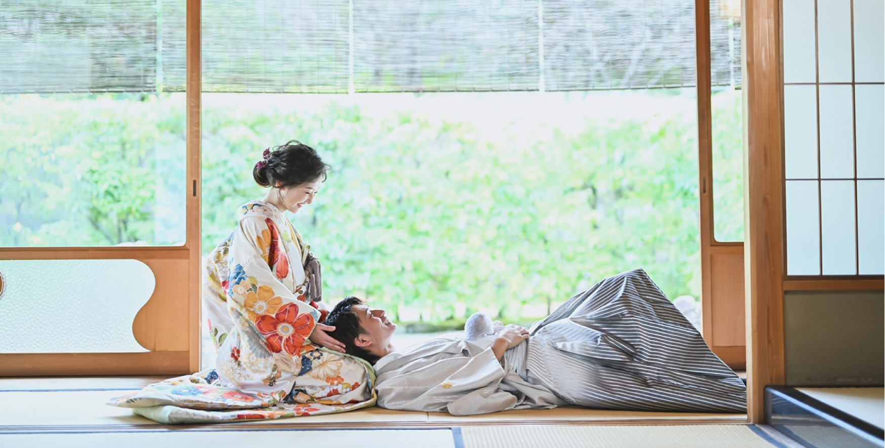 Bride cradling her groom's head in her lap as he reclines on tatami, laughing together beside a tea room's open garden view at Shirotori Garden.