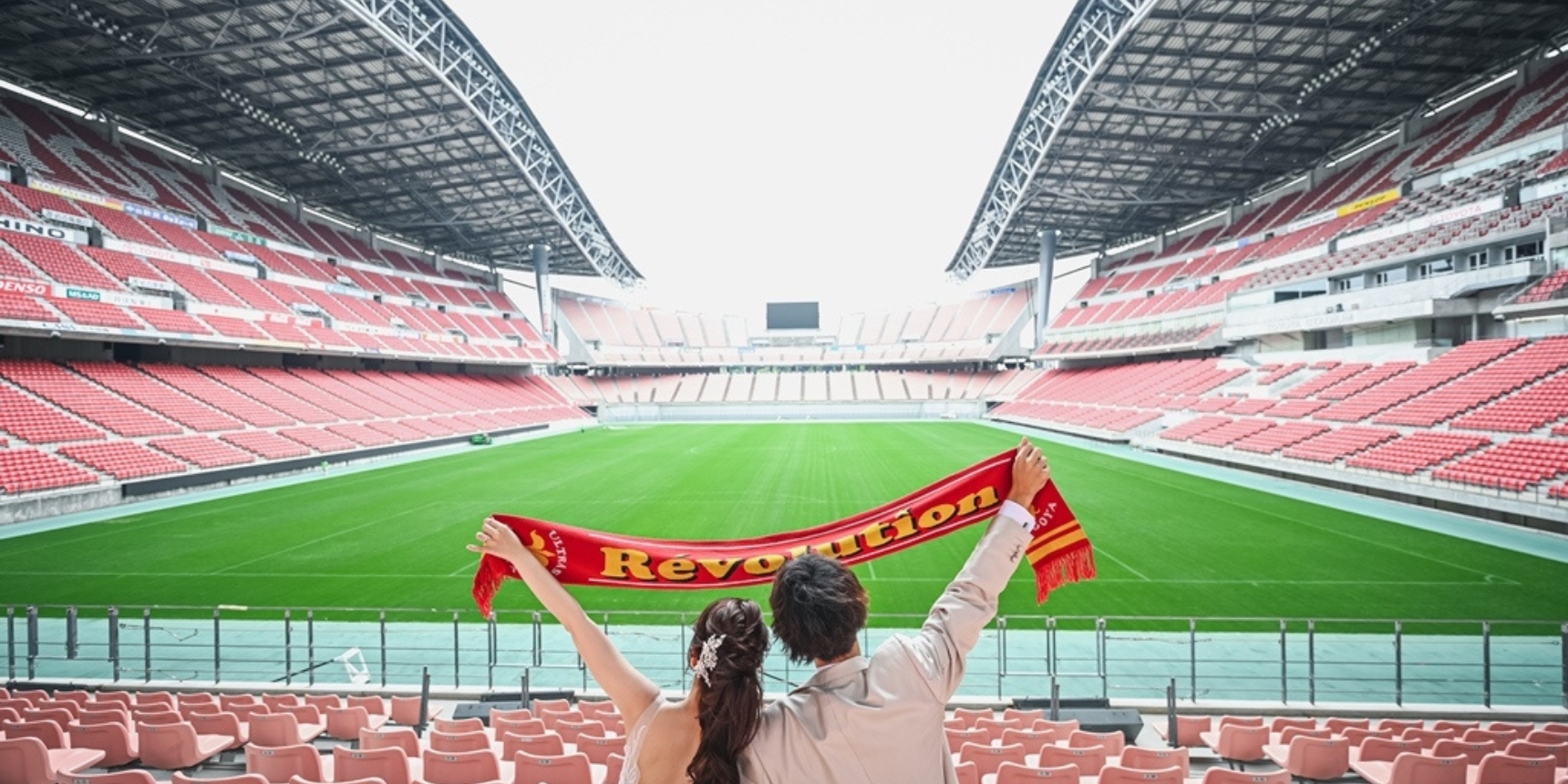 Couple seen from behind holding up a scarf overlooking an empty football stadium.