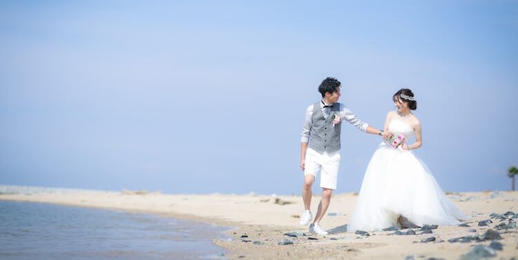 Walking hand in hand along the sandy shore of Rinku Beach, gentle waves lapping at the water's edge during their Japan wedding photography session.