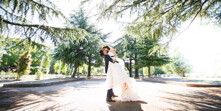 A romantic lift and kiss beneath towering pine trees at Tsuruma Park, one of Nagoya's most cherished gardens.
