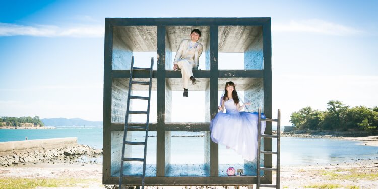 Perched playfully inside a giant art cube installation on Sakushima Island, the sea stretching out behind them.