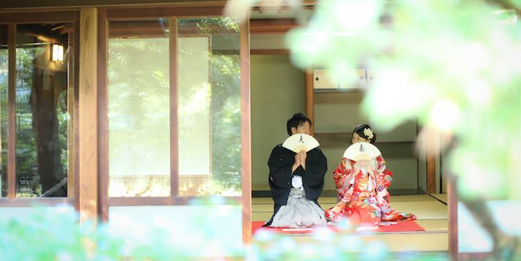 Playfully leading each other across the open lawns of Odaka Ryokuchi Park, a favorite Nagoya wedding photography spot framed by lush green trees under a clear blue sky.