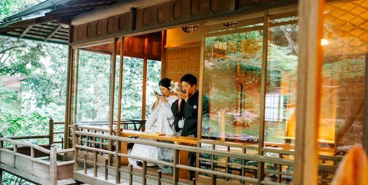 Sharing a quiet laugh on the glass-walled veranda of Furukawa Museum of Art, a serene setting for their wedding photography in Japan.