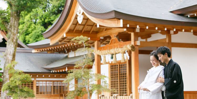 The bride and groom share a smile before the sacred shimenawa rope of Kounomiya Shrine's main hall.