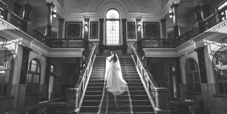 A striking black-and-white portrait of the bride descending the grand staircase inside the Nagoya City Archives building.