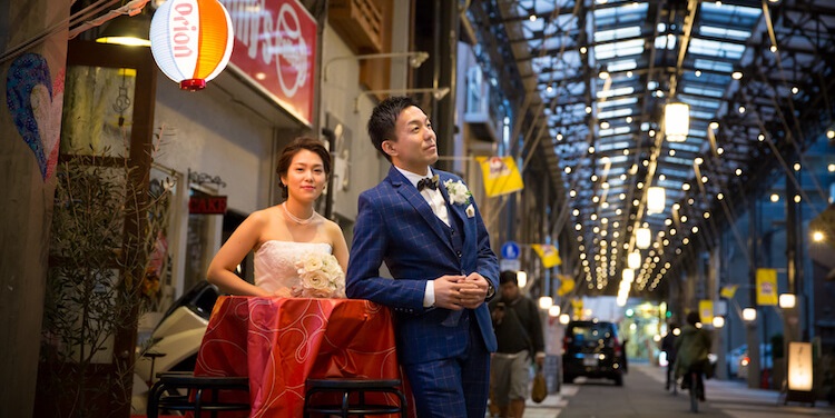 Couple standing beneath a lantern-lit covered shopping arcade at dusk, a rickshaw beside them.