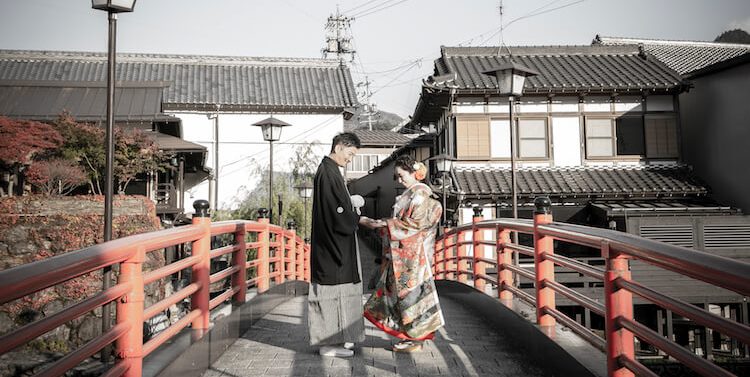 Meeting at the center of a vivid red bridge in the historic townscape of Gujo Hachiman during their Japan pre-wedding photoshoot.