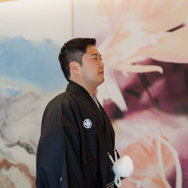 Profile of the groom in black montsuki hakama in front of a pastel floral mural, a solo portrait from a kimono wedding photoshoot