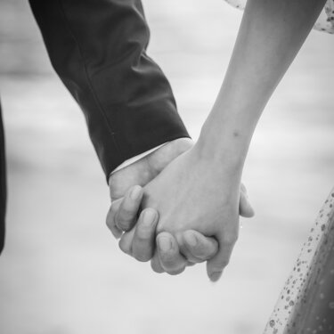 Black and white close-up of the bride and groom holding hands by the water, a simple detail shot from their wedding photos