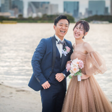 Laughing couple with the Tokyo skyline across the bay behind them at Odaiba Seaside Park, cheerful pre-wedding photography in Japan
