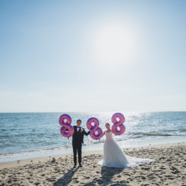 Couple holding giant pink number balloons on a sunny beach under a blue sky, a fun prop idea for a pre-wedding photoshoot in Japan