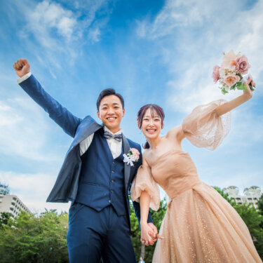 Low-angle shot of the couple cheering with arms raised under a bright blue sky, an energetic idea for wedding photos in Japan