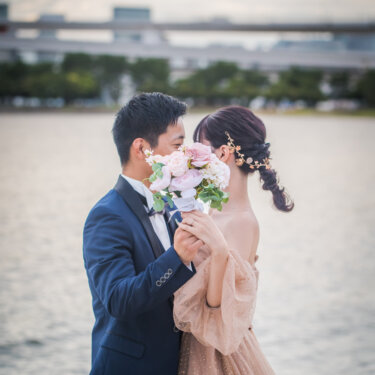 Bride and groom hiding a kiss behind a pink rose bouquet by the bay at Odaiba Seaside Park, romantic Japan wedding photography