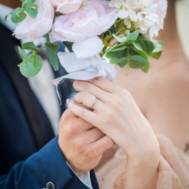 Close-up of the couple holding a pink rose bouquet together, showing the bride's ring, a detail shot for pre-wedding photos
