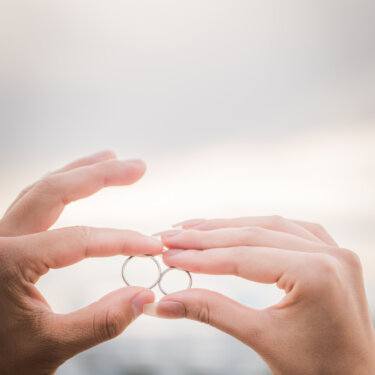 Bride and groom's fingertips holding their wedding rings against the soft sky over Tokyo Bay, a classic ring detail in wedding photos