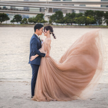 Groom holding the bride close as her blush tulle gown sweeps across the sand at Odaiba Seaside Park, flowing dress wedding photos in Tokyo