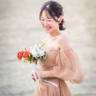 Smiling bride in a blush tulle off-shoulder gown holding a red and white bouquet by the water at Odaiba Seaside Park, Tokyo, during a pre-wedding photoshoot