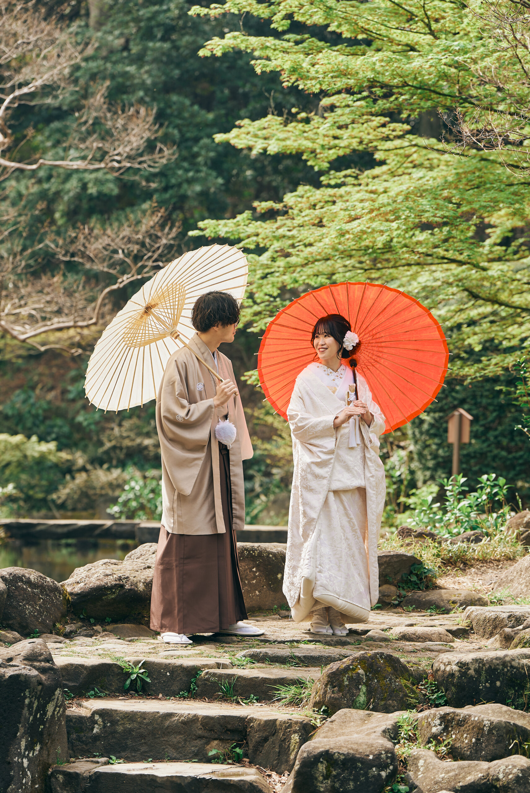 Kimono couple holding red and white Japanese umbrellas on the stone steps of Kansenen Garden during a pre-wedding photoshoot in Tokyo