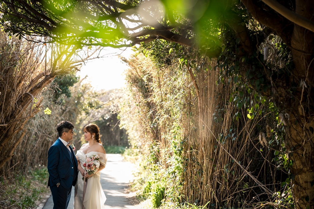 Bride and groom standing in a green tunnel of trees on Jogashima, natural light filtering through the leaves