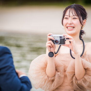 Bride in a sparkly blush gown laughing as she takes a photo of the groom with a retro camera, candid pre-wedding photography in Japan