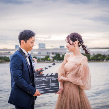 Couple holding a movie clapperboard by the water, a cinematic prop idea for a pre-wedding photoshoot at Odaiba Seaside Park