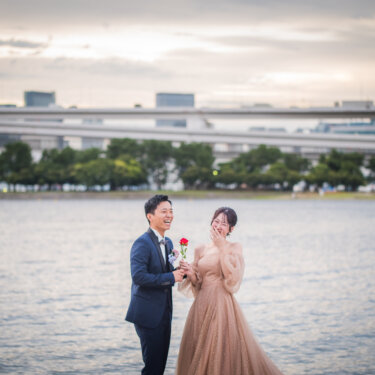 Groom handing a single red rose to his surprised bride on the shore of Odaiba, a sweet proposal-style moment in wedding photos in Tokyo