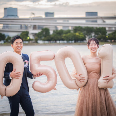 Bride and groom holding big blush number balloons on the beach in Tokyo, a creative idea for date-themed pre-wedding photos