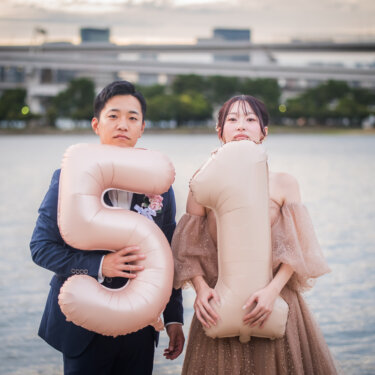 Couple posing with oversized number balloons as fun props in front of Tokyo Bay and the waterfront highway, playful Japan wedding photography