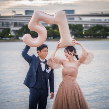 Bride and groom lifting number balloons above their heads and laughing at Odaiba Seaside Park during their pre-wedding photoshoot
