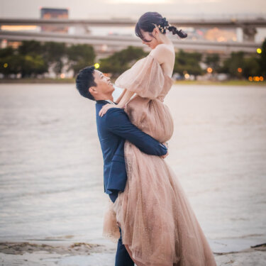 Bride lifted into the air by the groom on the beach at dusk, her blush tulle gown flowing, romantic wedding photos at Odaiba Seaside Park