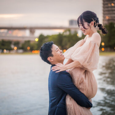 Groom hugging and lifting his laughing bride by the water at twilight, a joyful pose for a Japan wedding photoshoot