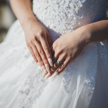 Close-up of the bride's hands with her wedding ring resting on the beaded lace bodice of her wedding dress, a detail shot from a pre-wedding photoshoot