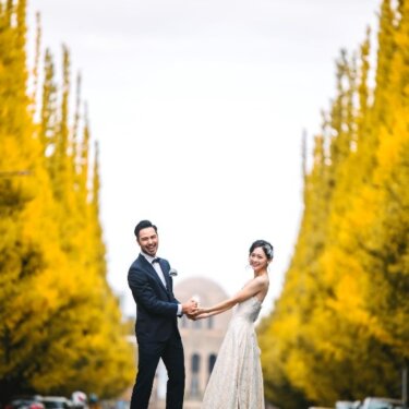The bride and groom hold hands under the golden ginkgo trees of Jingu Gaien Ginkgo Avenue, an autumn wedding photography spot in Tokyo