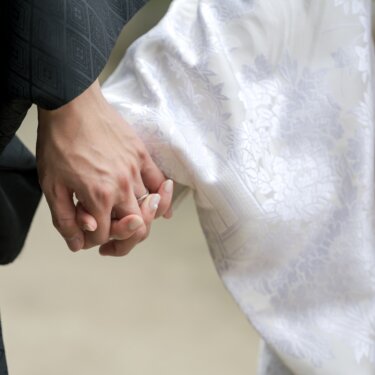 Close-up of the groom in black montsuki holding the bride's hand against her white shiromuku, wedding rings visible, a tender detail from a kimono wedding photoshoot