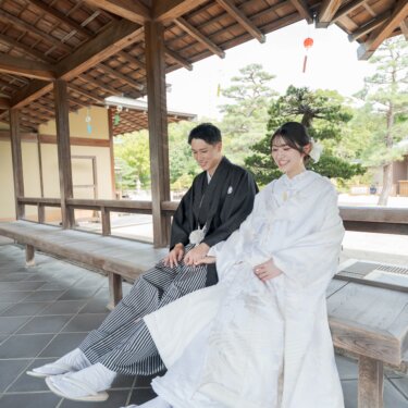 Bride and groom in shiromuku and striped hakama sitting side by side on a bench in the wooden corridor of Daisen Park Japanese Garden during their pre-wedding photoshoot
