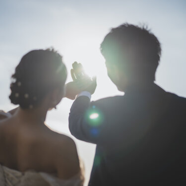 Couple seen from behind forming a heart shape with their hands against the bright sky, a backlit pose for seaside Japan wedding photography