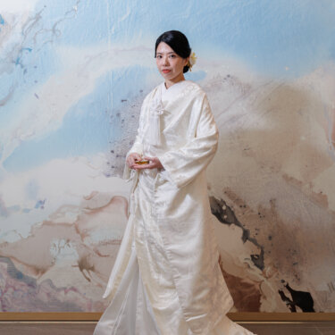 Full-length portrait of a bride in a silk shiromuku kimono in front of a blue and beige abstract mural, Japanese studio wedding photoshoot