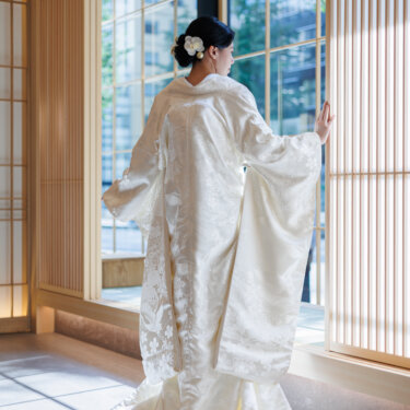 Back view of a bride in shiromuku with a long train, touching the lattice screen by a tall window, an elegant kimono wedding photography shot