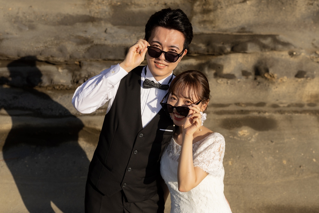 Wedding couple in matching sunglasses posing on the rocks of Jogashima, a fun resort-style wedding photo