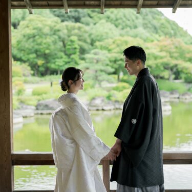 Groom in montsuki and bride in shiromuku holding hands and smiling at each other inside a lakeside pavilion at Daisen Park, a quiet moment from their Japan wedding photography session