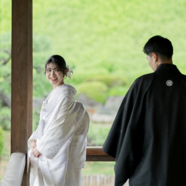 Bride in shiromuku glancing back with a smile at the groom in black montsuki on the garden pavilion, a playful look-back pose for a pre-wedding photoshoot in Japan
