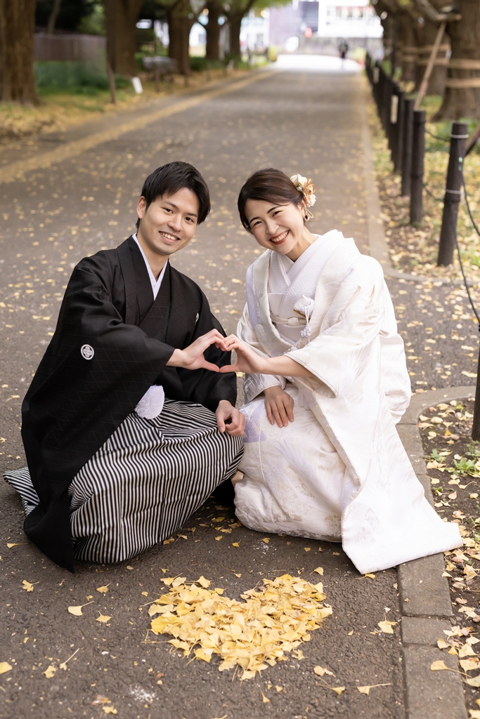 Kimono couple sitting behind a heart made of fallen ginkgo leaves and making a heart shape with their hands at Jingu Gaien