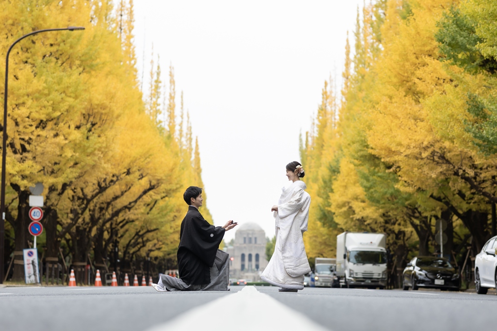 Groom in montsuki hakama kneeling to recreate his proposal to the bride in shiromuku on the Jingu Gaien Ginkgo Avenue