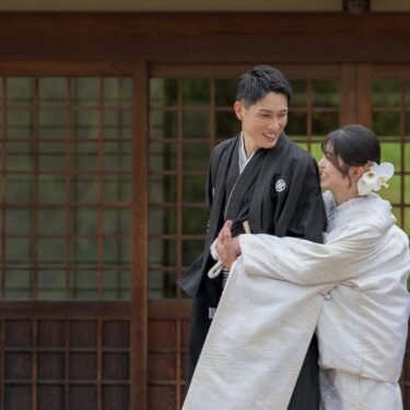 Bride in shiromuku hugging the groom in montsuki in front of latticed sliding doors, both smiling, a sweet hug pose for kimono wedding photos